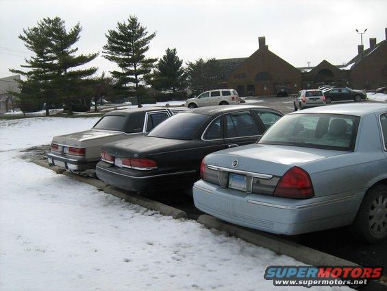 Three sedans parked in snow, one light blue, one black, and one beige. The light blue sedan is in the foreground