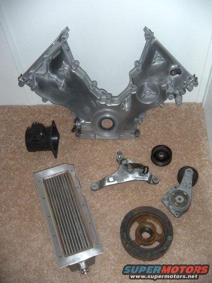 Engine timing cover, intake manifold, oil cooler, belt tensioner, and pulley assembly laid out on carpet