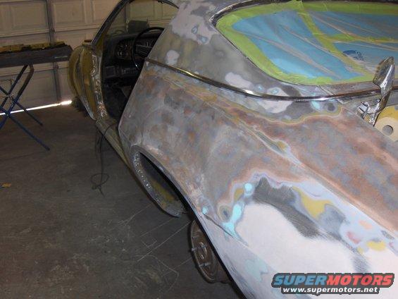 Side view of a car body undergoing repair, showing primer and body filler