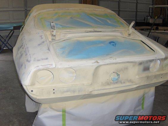 Car body covered in primer, rear view. Trunk and windows are masked off