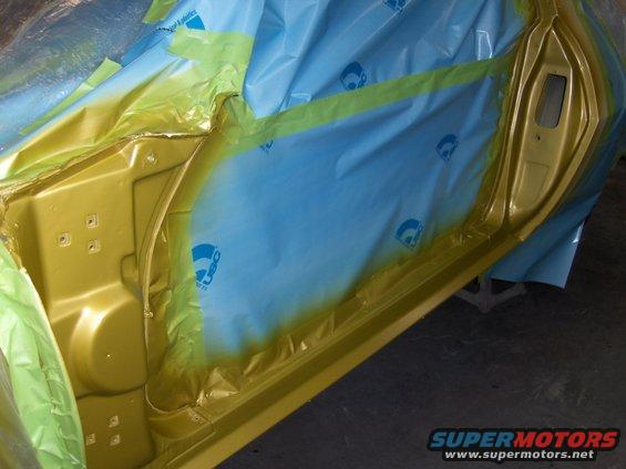 Car door interior masked with blue plastic and yellow tape, showing exposed metal