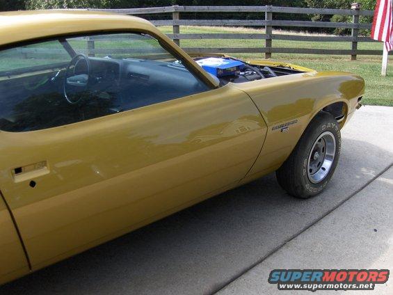 Yellow coupe with hood open, showing interior and engine bay. American flag visible in background