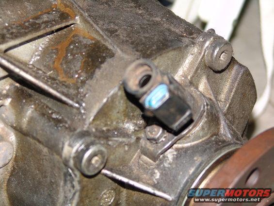Close-up of a transmission speed sensor attached to a greasy metal housing