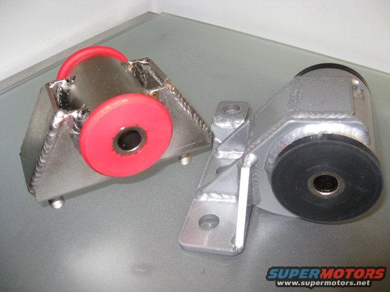 Two metal engine mounts with red and black rubber bushings on a grey surface. One mount has red bushings and is on the left. The other mount has black bushings and is on the right