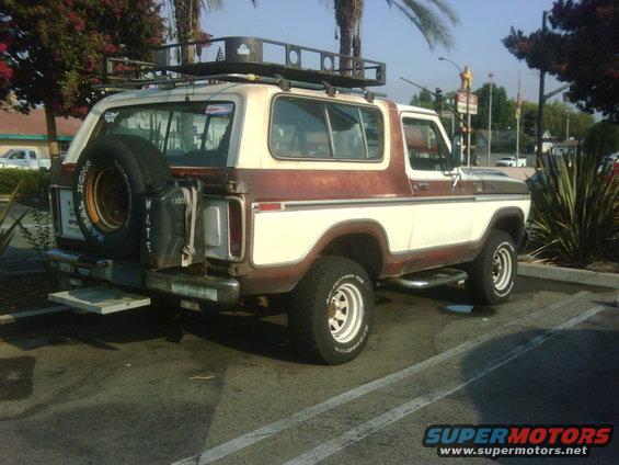 Two-tone brown and white Ford Bronco with a roof rack and spare tire on the back