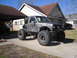 1984 Ford Bronco II - Modified pickup truck with oversized tires and a custom roll cage sits in a suburban driveway.