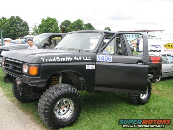 Black lifted 1986 Ford Bronco with 'Trail Smith 4x4 LLC' and '3406' decals, parked on grass
