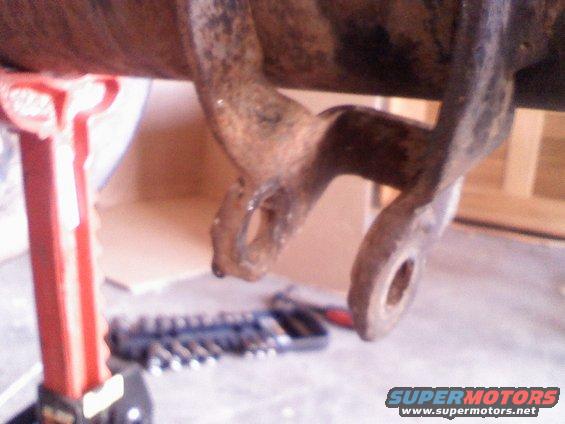 rusted metal bracket with holes, supported by a red jack stand, with tools on the floor