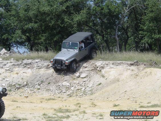 Silver Jeep Wrangler driving off-road on a rocky incline