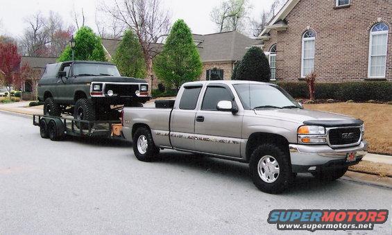 Dark green Ford Bronco on a trailer, towed by a silver GMC Sierra pickup truck