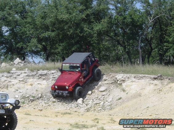 Red Jeep Wrangler climbing a rocky hill with a white vehicle to the left