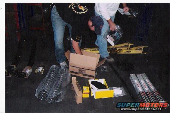 Two people unpack car parts including coil springs and boxed components