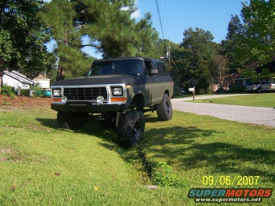 Dark green and black lifted 1978 Ford Bronco with aftermarket grille and large tires parked on a grassy incline