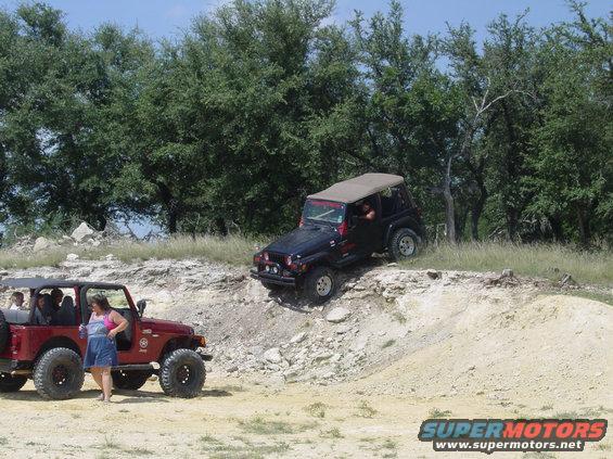 Red Jeep parked on dirt, black Jeep climbing a rocky incline
