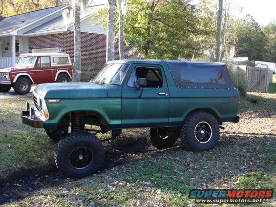 Lifted green Ford Bronco with soft top parked next to a red Ford Bronco