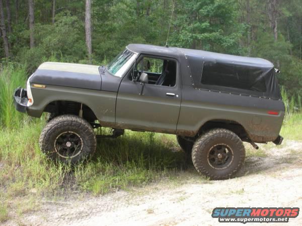 Olive green and black 1978 Ford Bronco with a soft top, lifted suspension, and off-road tires on a dirt path