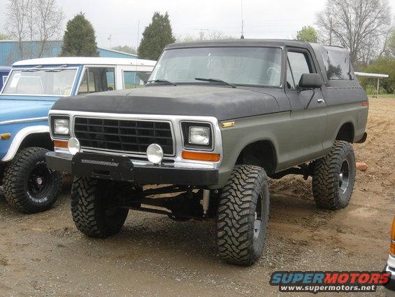 Lifted 1978 Ford Bronco with large off-road tires parked next to a blue vehicle