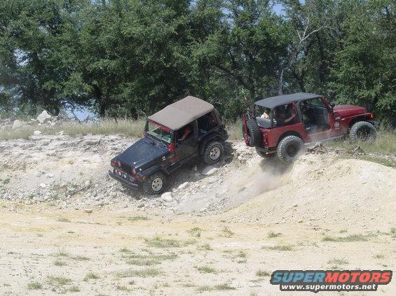 Two Jeeps, one black and one red, navigating a dirt hill off-road