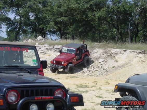 Several Jeeps on a rocky, off-road trail with trees in the background. One Jeep has 'got mud?' on its bumper