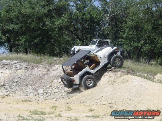 Two white Jeeps climbing a dirt hill off-road. One Jeep is in the foreground, angled up the slope