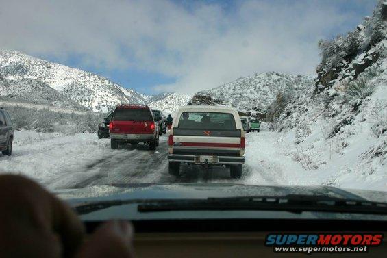 White Bronco in traffic jam on snowy road, mountains in background