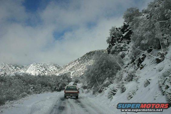 White and red pickup truck driving on a snowy mountain road