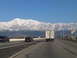 1986 Ford Bronco - A highway stretches towards snow-capped mountains under a clear blue sky, with several vehicles on the road.