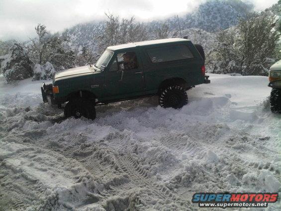 Green 1986 Ford Bronco stuck in deep snow, with another vehicle partially visible