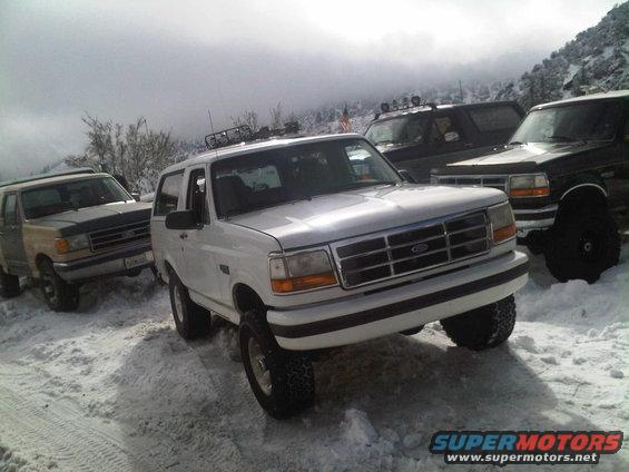 White Ford Bronco in snow, front 3/4 view. Other Broncos visible