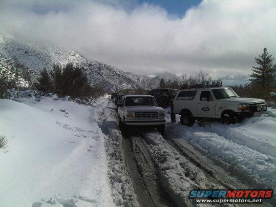 White Ford Bronco with roof rack and off-road lights on a snow-covered road