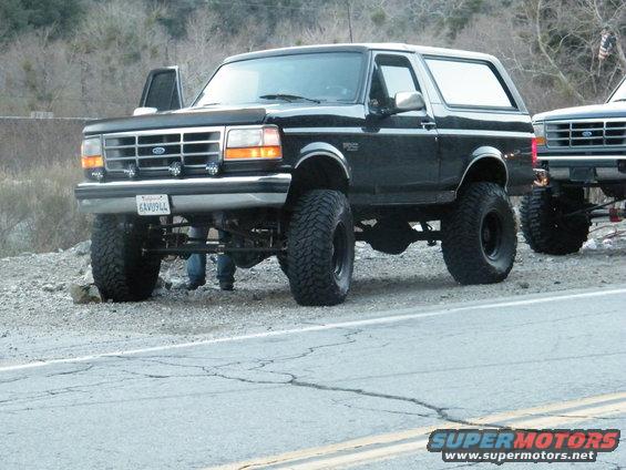 Lifted black Ford Bronco parked on roadside, another Bronco visible to the right