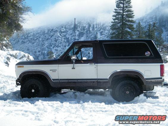 Two-tone brown and white Ford Bronco stuck in snow, side view