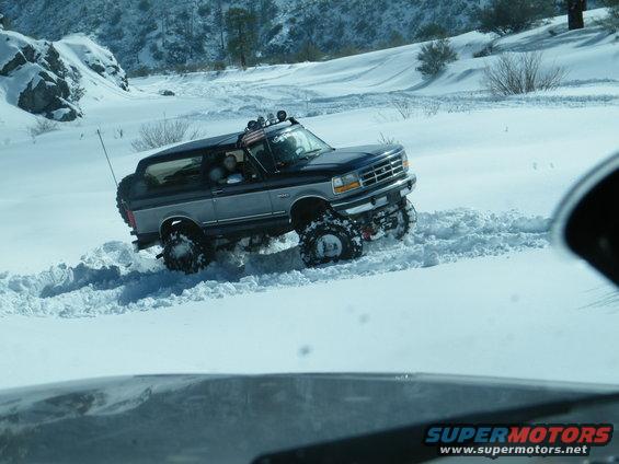 Blue and silver SUV with off-road tires driving through deep snow. Appears to be a 1992-1996 Ford Bronco