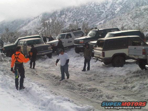 Several SUVs and trucks parked in snow, some with people around them. A white and brown SUV is in the foreground