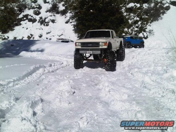 White 1987 Ford F-150 pickup truck with large off-road tires in snow