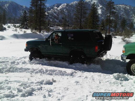 Green Ford Bronco with spare tire on rear, driving in snow
