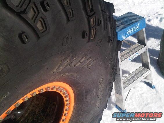 Large off-road tire with orange beadlock wheel and a blue step stool in snow