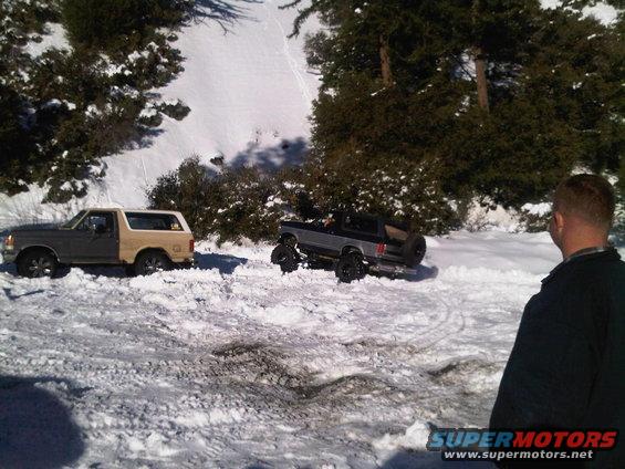 Two Ford Broncos stuck in snow, one gray and tan, the other black with off-road tires