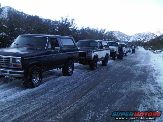 Black 1980 Ford Bronco in a line of SUVs on a snowy road