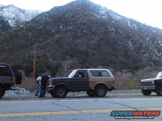 Two-tone Ford Bronco parked on roadside, another Ford truck visible to the right