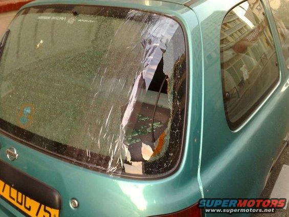 Green car's rear window is shattered and taped over. A yellow license plate is partially visible