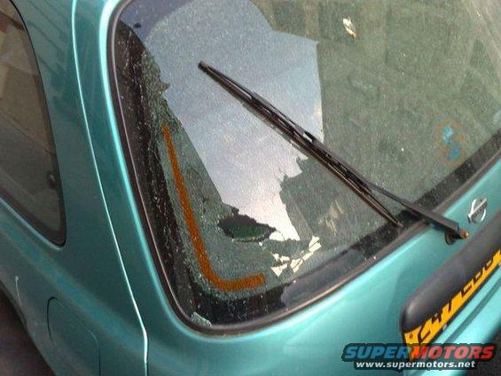 Teal hatchback rear window with wiper and cracked glass. Yellow text on bumper
