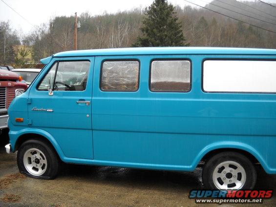 Blue van with a flat front tire and aftermarket wheels, seen from the side