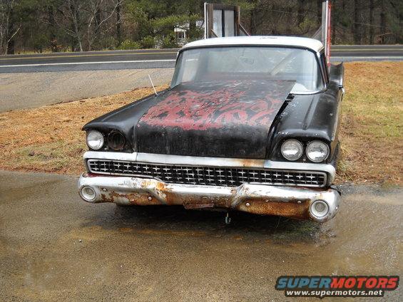 Black and white car with red distressed hood, rusty chrome bumper, and dual headlights
