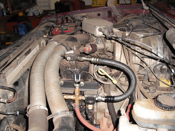 Engine bay showing large intake hoses, fuel lines, and various engine components. Aftermarket parts are visible