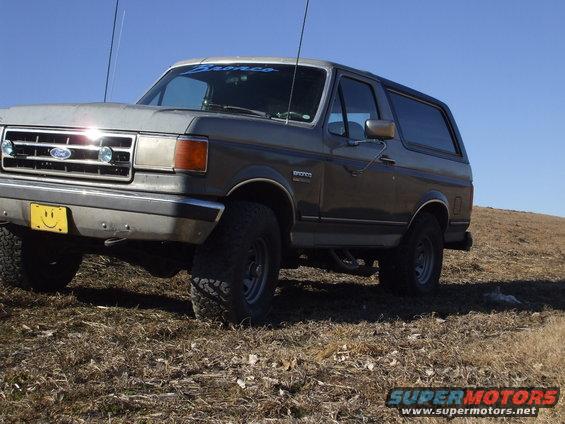 Gray 1989 Ford Bronco with a smiley face license plate parked on a grassy hill