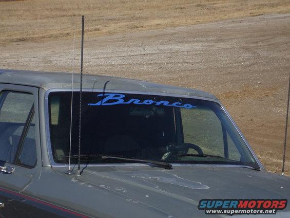 Gray Ford Bronco with blue 'Bronco' decal on windshield. Two antennas visible