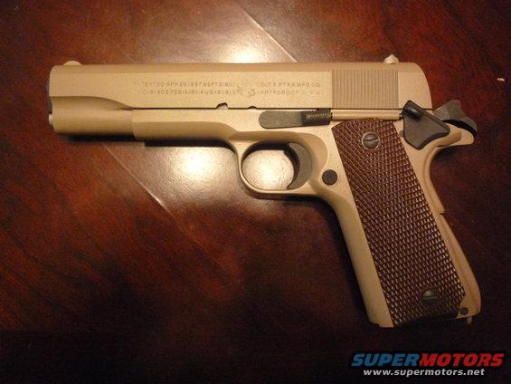 Colt 1911 pistol with tan finish and brown grips on a wooden surface
