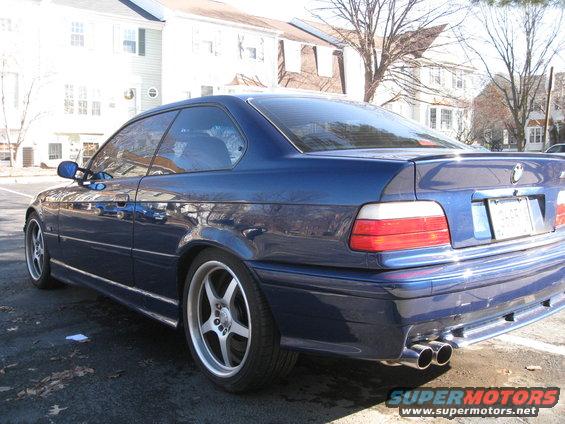 Blue coupe with aftermarket five-spoke wheels, dual exhaust, and a rear spoiler. The car is parked on asphalt