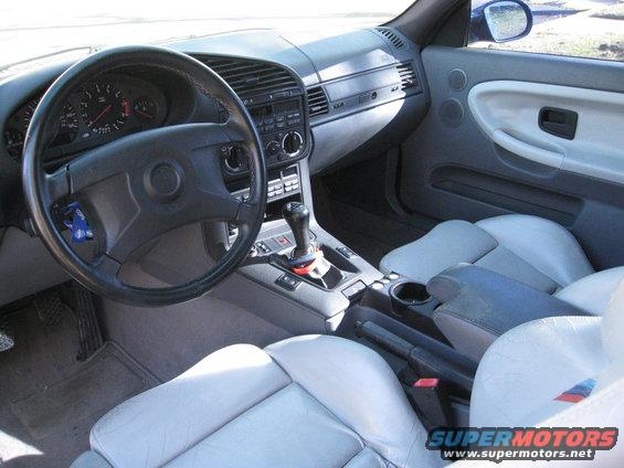 Interior of a BMW with light grey seats, black steering wheel, and center console with a manual shifter